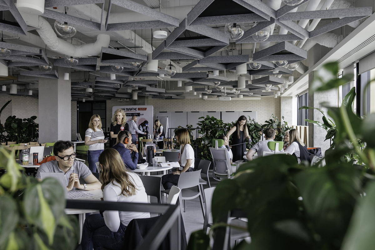 Participants in the event talk and perform tasks at tables in the Leroy Merlin office space. In the background is the “Change perspective with Agates” board and educational stations.